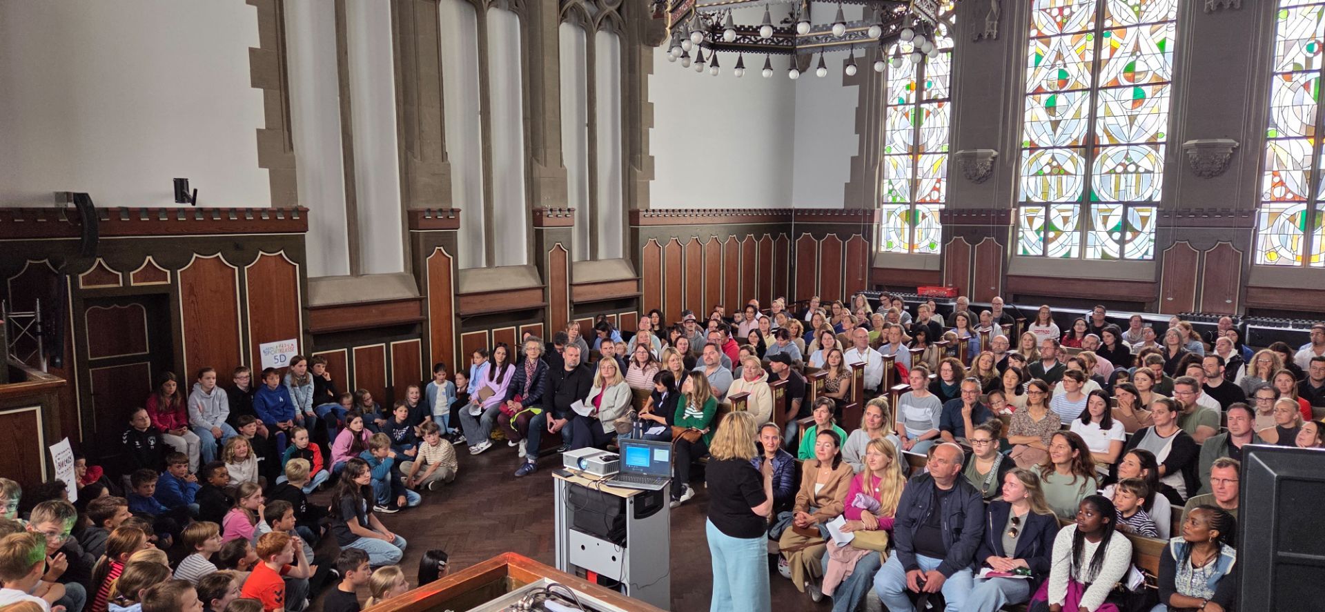 Frau Winter begrüßt Kinder und Eltern in der Aula.jpeg